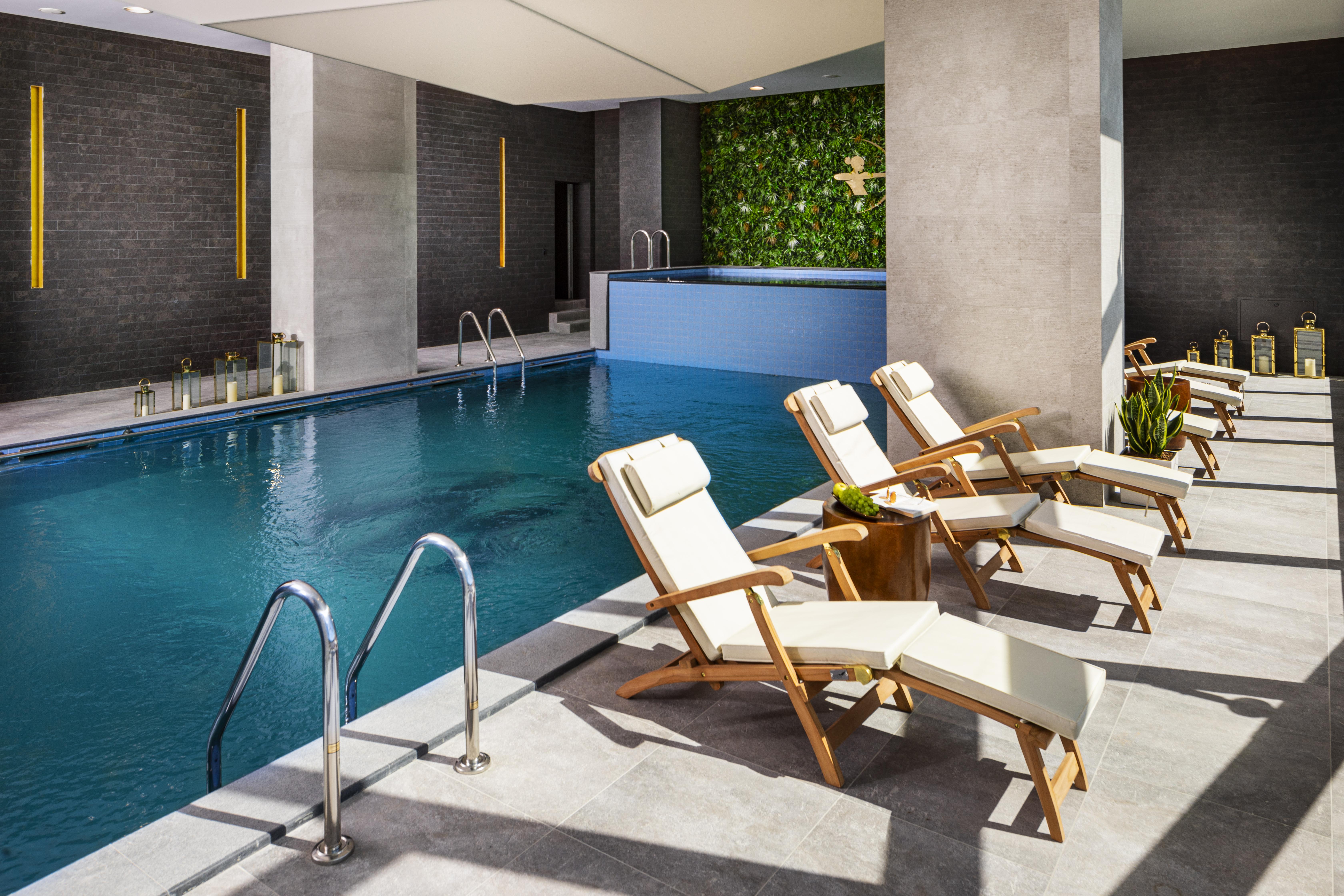 Grand Hotel Millennium Sofia Exterior photo The photo shows a serene indoor swimming pool area. The pool is clear and inviting, with a blue water surface reflecting light. Along one side of the pool, there are several light-colored lounge chairs with white cushions, positioned for relaxation. 
