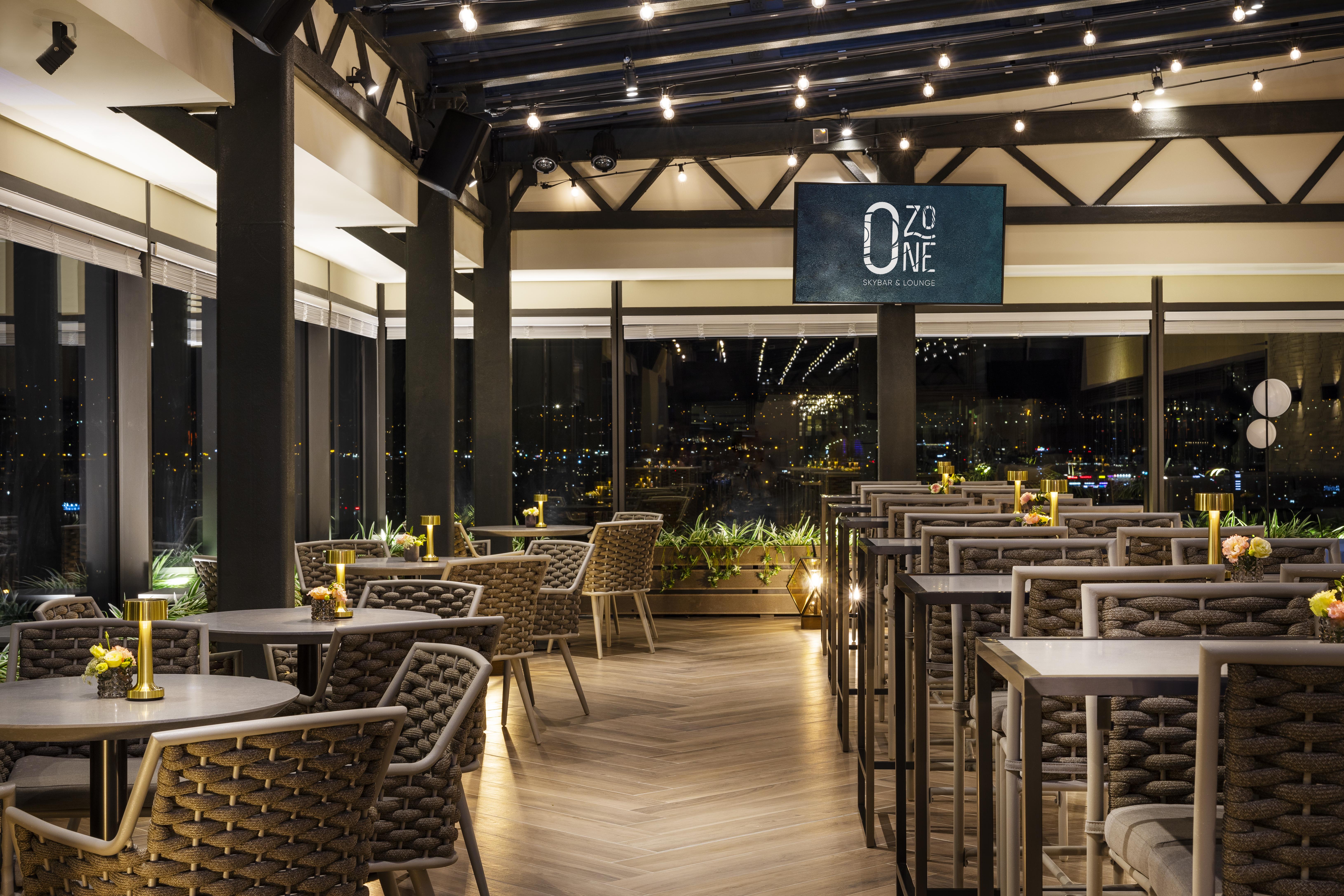 Grand Hotel Millennium Sofia Exterior photo The photo depicts a modern restaurant interior with a stylish design. The space features a series of tables and chairs arranged neatly, with a clean and sophisticated aesthetic. The tables are set with small yellow flowers, adding a touch of color to